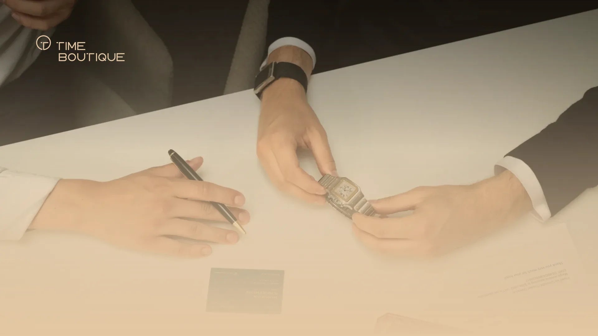 A watch being handed over at a table with pen and papers